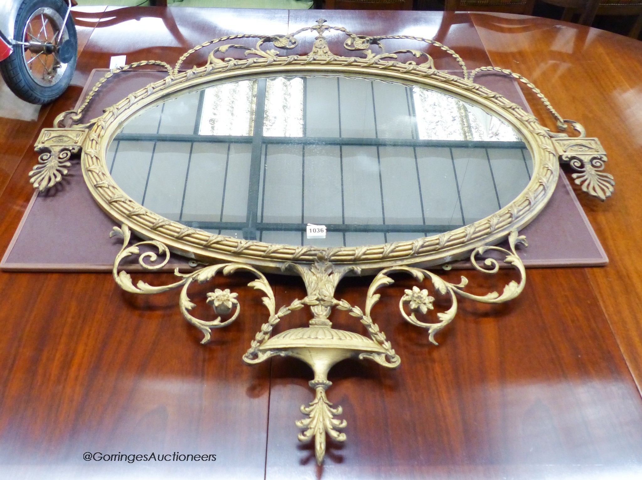 A 19th century regency style oval gilt wood and gesso wall mirror with urn finial. W-113, H-116cm.